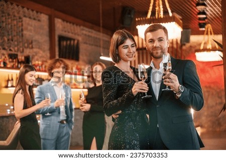Man with woman is posing. Group of people in beautiful elegant clothes are celebrating New Year indoors together.