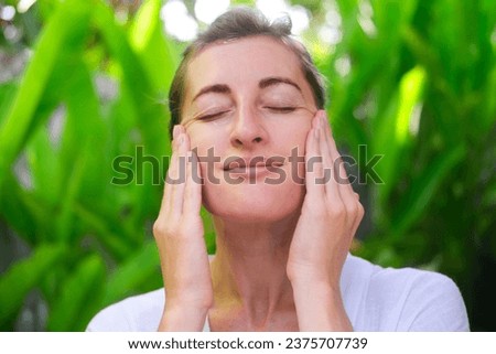 Close up photo of a middle-aged woman doing a facial massage using massage cream. Daily skin care and fight against age-related changes. Facial skin care at home.