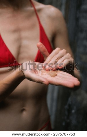 Vertical photo of a woman in the shower squeezing shower gel out of a jar and soaping her hands. Foam from shower gel and soap texture in woman's palms. Daily hygiene, caring for your body.