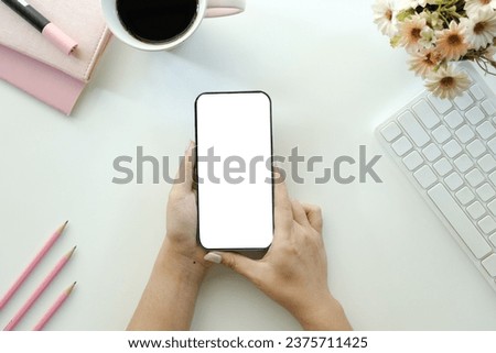Cropped shot top view of businesswoman hands using smartphone mockup at the white office desk. Blank screen mobile phone for graphic display montage.