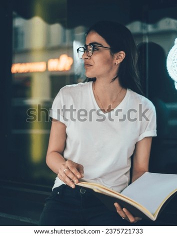 Calm pensive confident woman with papers against shop window with big silver clock in downtown