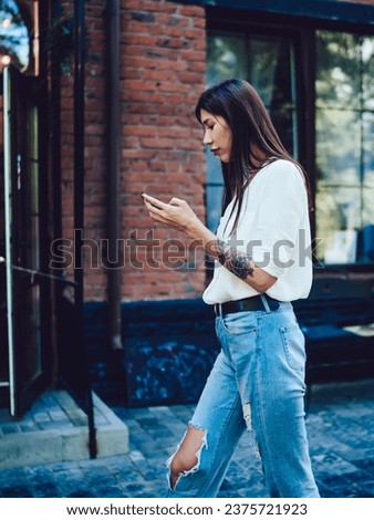 Side view of millennial female blogger installing medial application to smartphone device