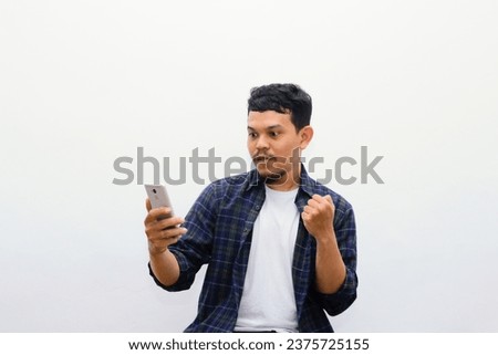 Portrait of attractive Asian man in casual shirt playing games on his mobile phone. Wow expression. Isolated image on white background