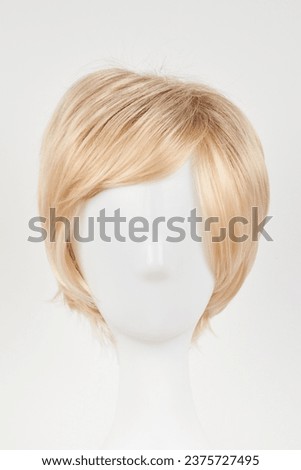 Natural looking blonde fair wig on white mannequin head. Short hair cut on the plastic wig holder isolated on white background, front view
