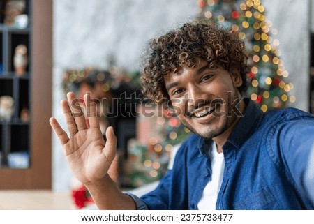 Happy and smiling cheerful man looking at phone camera talking with friends and family from a distance sitting on sofa in living room, web camera view, celebrating new year and christmas near tree.