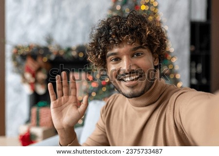 Happy and smiling cheerful man looking at phone camera talking with friends and family from a distance sitting on sofa in living room, web camera view, celebrating new year and christmas near tree.
