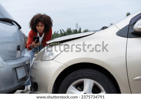Half Thai African driver check for damage after a car accident before taking pictures and sending insurance. Online car accident insurance claim after submitting photos and evidence to an insurance.