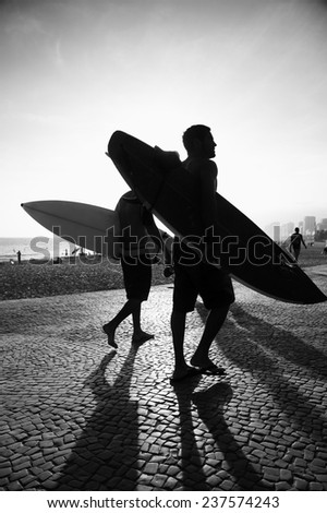 Sunset silhouettes of surfers walking at Arpoador Ipanema Beach Rio de Janeiro Brazil in black and white