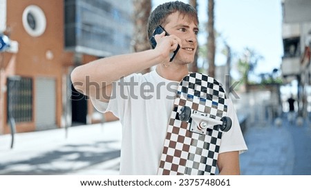Young caucasian man talking on smartphone holding skate at street