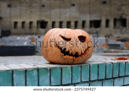 Halloween. A large orange pumpkin with holes for eyes and a mouth stands on a blue brick wall. ruins in the background