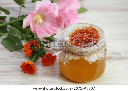 Natural herbal ointment, filtered medicinal cream from  marigold flowers.  Calendula cream good for better skin, Calendula officinalis  in front,  Alcea rosea at back.