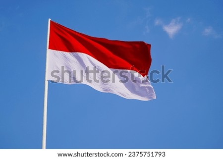 
The red and white national flag of Indonesia with cloth material flutters in the wind above the sky.