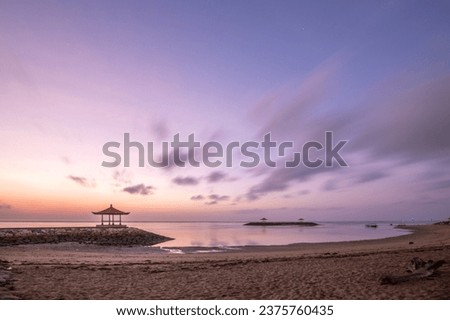 Magical sunrise with clouds in the sky. Dramatic sky at Sanur beach, Denpasar in Bali. Temple in the calm sea in the morning. Tropical landscape shot