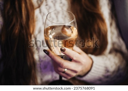 Woman drinking wine. White wine drinking. Wine glass in hand. Girl in woolen sweater. Cozy winter alcohol background. Female hand holding wine glass. Winter season clothing. Shallow depth of field.