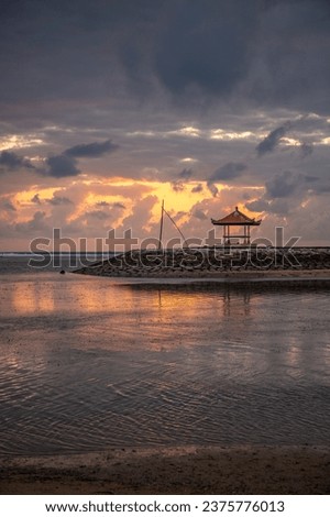 Beautiful sunrise on Sanur beach. Temple in the calm sea. Small waves in the morning. Sandy beach on the dream island of Bali. Sunset in a landscape shot, looking into the horizon