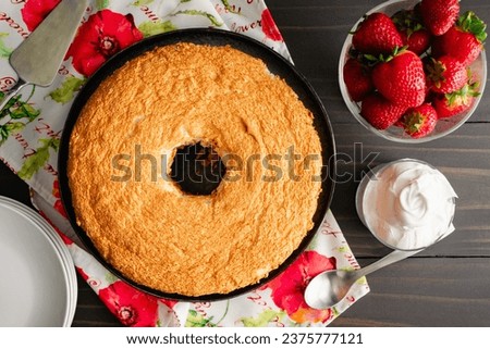 Angel Food Cake with Strawberries and Whipped Cream on the Side: Overhead view of a whole unsliced sponge cake with fresh berries, whipped topping
