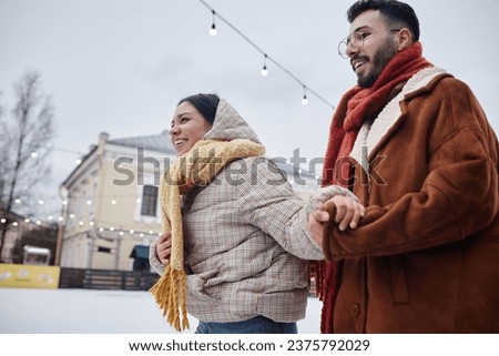 Side view at happy young couple ice skating together outdoors in winter and smiling, copy space