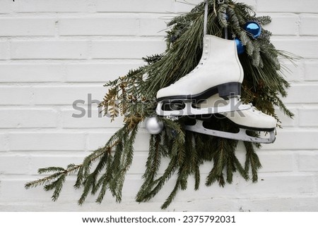 Minimal background image of ice skates with pine tree wreath on white wall, Christmas season, copy space