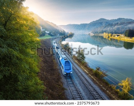 Aerial view of blue modern high speed train moving near river in alpine mountains in fog at sunrise in autumn. Top view of train, railroad, lake, reflection, trees in fall. Railway station in Slovenia Royalty-Free Stock Photo #2375793673