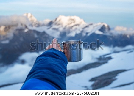Young woman holding a metal hot tea cup during sunset time from the Mera Peak high camp with snowy seven-thousander mountains. Climbing expedition acclimatization. Active people concept.