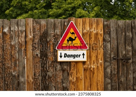 A warning sign about the danger of wild animals hangs on a wooden fence. Close-up