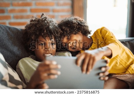 Little African American kids relaxing on sofa at home and watching something on digital tablet