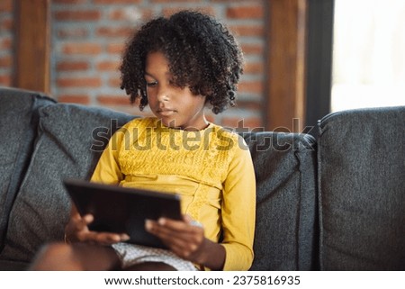 Little African American girl watching cartoons on touchpad at home