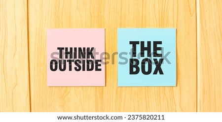 Inscription THINK OUTSIDE THE BOX on pink and blue square sticky sticker on wooden wall
