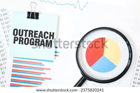 Green card on the white notepad and magnifier on the financial documentation. Text OUTREACH PROGRAM. Business concept Royalty-Free Stock Photo #2375820241