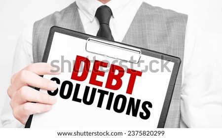 DEBT SOLUTIONS inscription on a notebook in the hands of a businessman on a gray background, a man points with a finger to the text