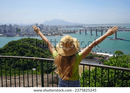 Joyful girl visiting Brazil. Beautiful young woman with raised arms enjoying view of Vitoria cityscape the capital of Espirito Santo state in Brazil. Royalty-Free Stock Photo #2375825245