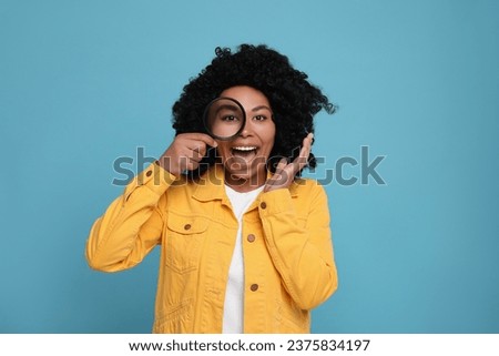 Emotional woman looking through magnifier glass on light blue background