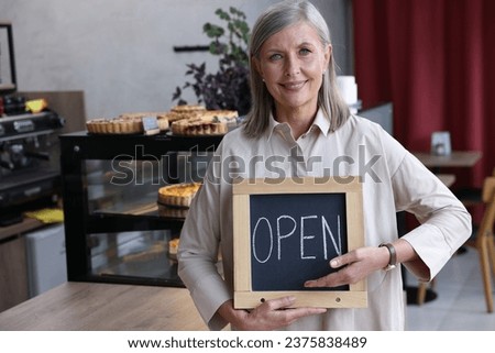 Happy business owner holding open sign in her cafe, space for text