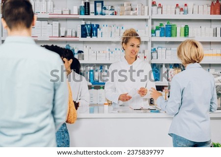 Portrait of confident female pharmacist working in a drugstore and talking with a senior patient customer while selling and putting prescription medications in a bag. Busy day in a pharmacy. Royalty-Free Stock Photo #2375839797