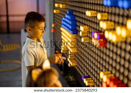 Kids making a picture with colored chips on the wall, playing on interactive models in science museum. Concept of children's entertainment and learning