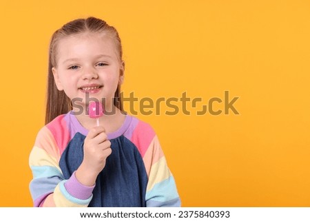 Happy little girl with lollipop on orange background, space for text Royalty-Free Stock Photo #2375840393