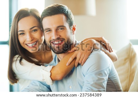 Enjoying every minute together. Beautiful young loving couple sitting together on the couch while woman embracing her boyfriend and smiling  Royalty-Free Stock Photo #237584389