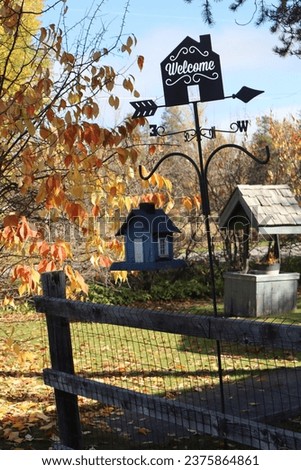 House shaped welcome sign and birdhouse in front yard during fall with well in background
