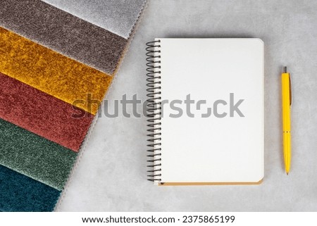 Colorful textile samples, notepad and pen on white table. Fabric swatches, set in different colors for selection. Variety of upholstery material for furniture and interior.