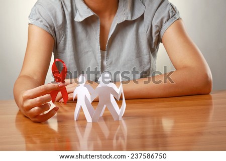 Female hands holding paper people and a red hiv ribbon, closeup