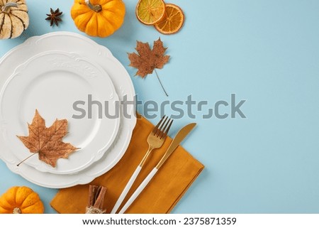 Develop a table setting that lingers in memory. Top view photo of crockery, pumpkins, dry orange slices, napkin, maple leaves, traditional fall elements on light blue background with promo zone
