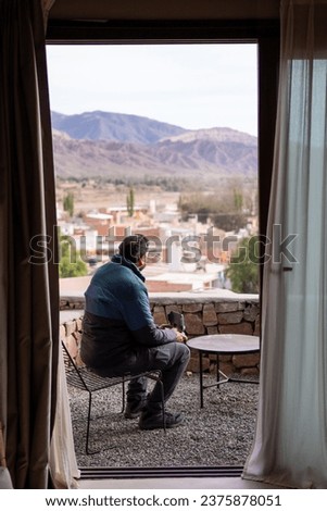 Drone pilot sitting on the balcony of a hotel room using the drone controller to take a shot from outside with a desert landscape in northern Argentina. Vertical shot from inside the hotel.