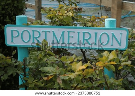 The beautiful and tastefully done, stylized Entrance Sign Post for the beautiful Italian Style Village Portmeirion, in Turquoise and White Colours. The Signpost is surrounded with lush Green Leaves.