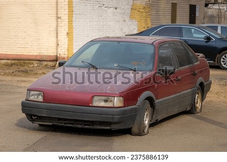 An old abandoned broken car with flat tires on the city parking. The scrap and recycling vehicle. The dusty and rusty machine body and the broken headlight Royalty-Free Stock Photo #2375886139