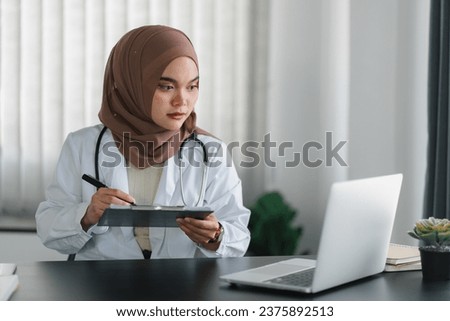 Young muslim female doctor in brown hijab headscarf working with medical papers while sitting in modern clinic office