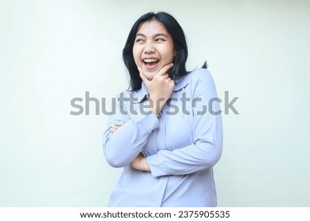 portrait of carefree asian young business woman looking aside excited with hand on chin and folded arm wearing formal purple suit isolated in white background