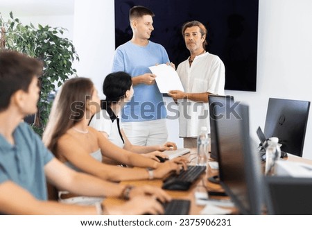 Among students of computer courses, man teacher awards diploma patent and presents document to excellent guy student Royalty-Free Stock Photo #2375906231