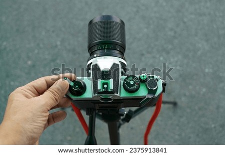 A hand was turning a film loader of a vintage film camera with black lens on road surface background with a tripod, retro and travel vintage concepts.