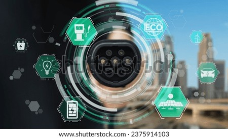Focus EV charger pointing in front of camera display eco-friendly pictogram hologram with blur esg green city background. EV car charger using alternative clean energy reducing CO2 emission.Peruse