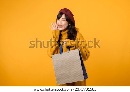 Young Asian woman 30s, wearing a yellow sweater and red beret, enjoys discount shopping and shouting to free copy space against a vibrant yellow backdrop.